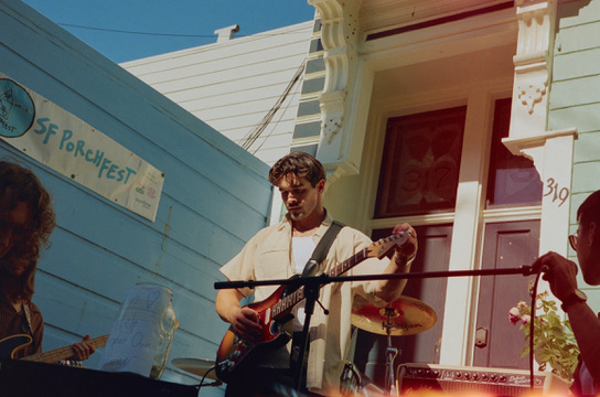 Sunkissed's frontman at the mic with a red guitar during their SF Porchfest set