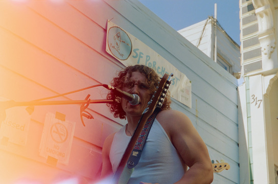 Vocalist singing into the mic under a sun-flared sky at SF Porchfest