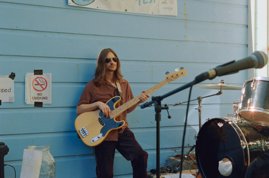 Bassist leaning against a blue Victorian wall during SF Porchfest