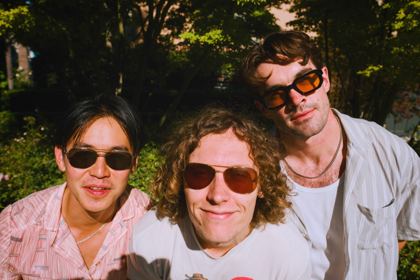 Three of the band in sunglasses, sunlit close-up portrait