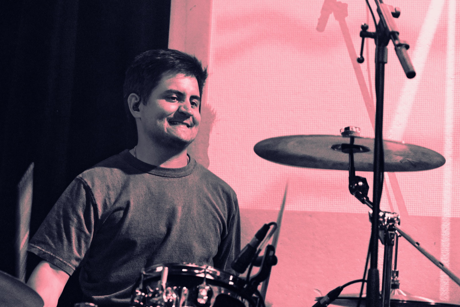 Drummer smiling behind the kit under pink light