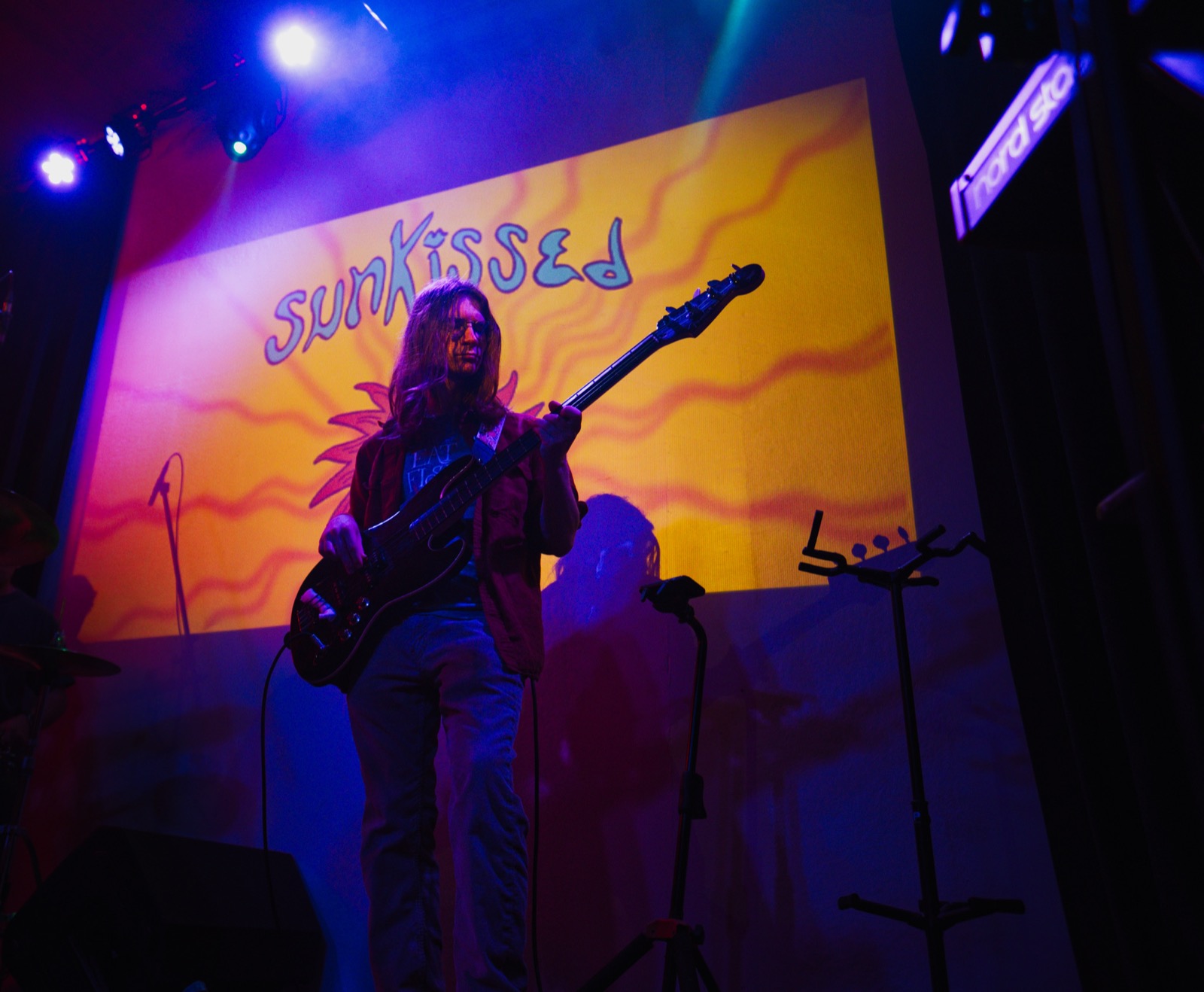 Bassist performing on stage with sunkissed banner